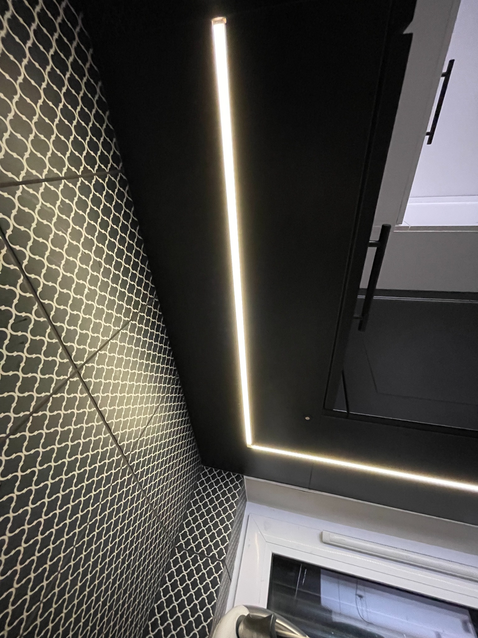 Nowoczesna kuchnia z czarnymi szafkami i podświetleniem LED, wzorzysta ściana z płytek.