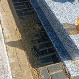 Ułożona kostka brukowa wokół nagrobka, zasypana piaskiem, widoczne elementy nagrobka z granitu.