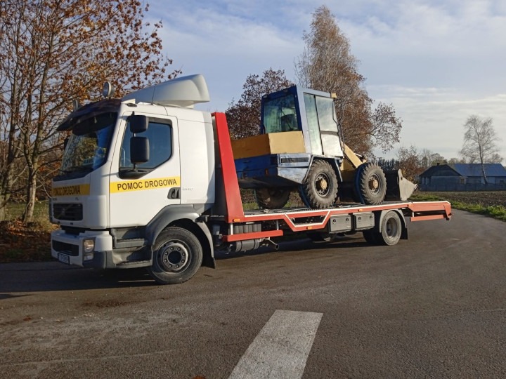 Laweta przewozi ładowarkę kołową na tle jesiennego krajobrazu wiejskiego.