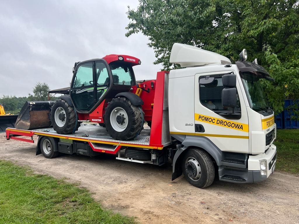 Czerwony wózek widłowy Manitou z łyżką transportowany na lawecie pomocy drogowej, widok z boku na szutrowej drodze.
