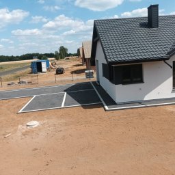 Mistral - A Zarzycki Sp. Jawna - Nowoczesny dom jednorodzinny z szarą kostką brukową na podjeździe i wokół budynku, w tle widoczny kontener i inne domy w trakcie budowy.