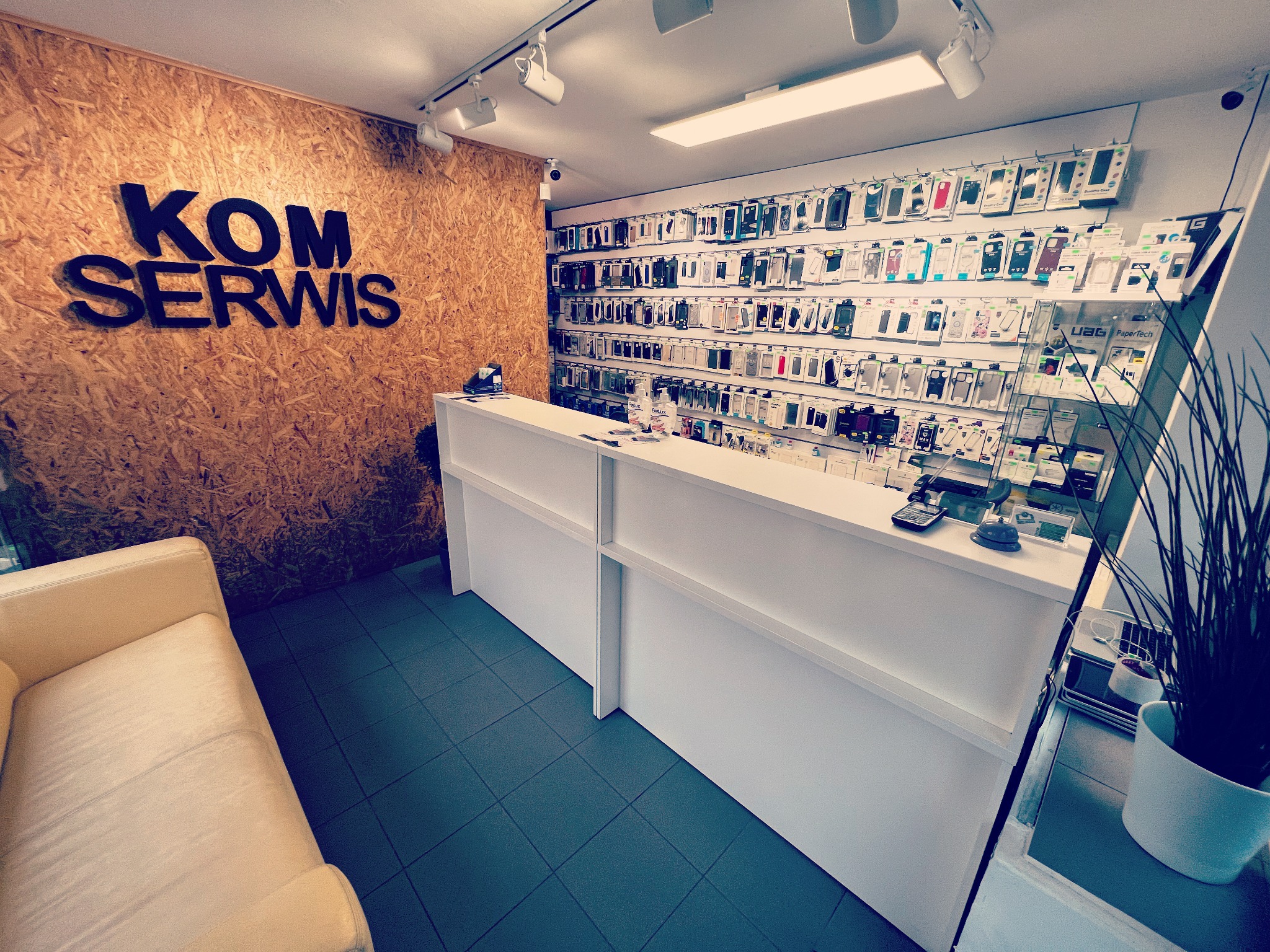 Wnętrze serwisu komputerowego w Warszawie z widoczną ladą obsługi, ścianą z ekspozycją etui na telefony i sofą dla klientów.
