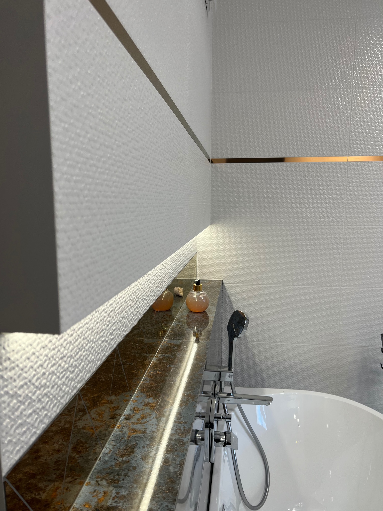 Nowoczesna łazienka z białymi płytkami o fakturze, złotymi listwami, marmurowym blatem podświetlonym LED i wolnostojącą wanną