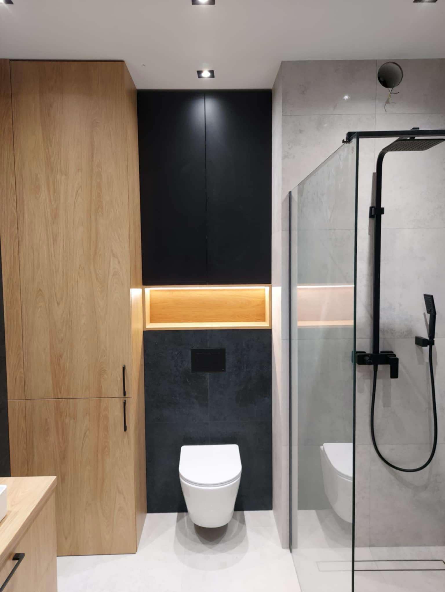 Nowoczesna łazienka z drewnianymi szafkami, czarnymi akcentami i kabiną prysznicową typu walk-in, oświetlenie LED podkreśla ciepłe drewno i chłodne szarości.