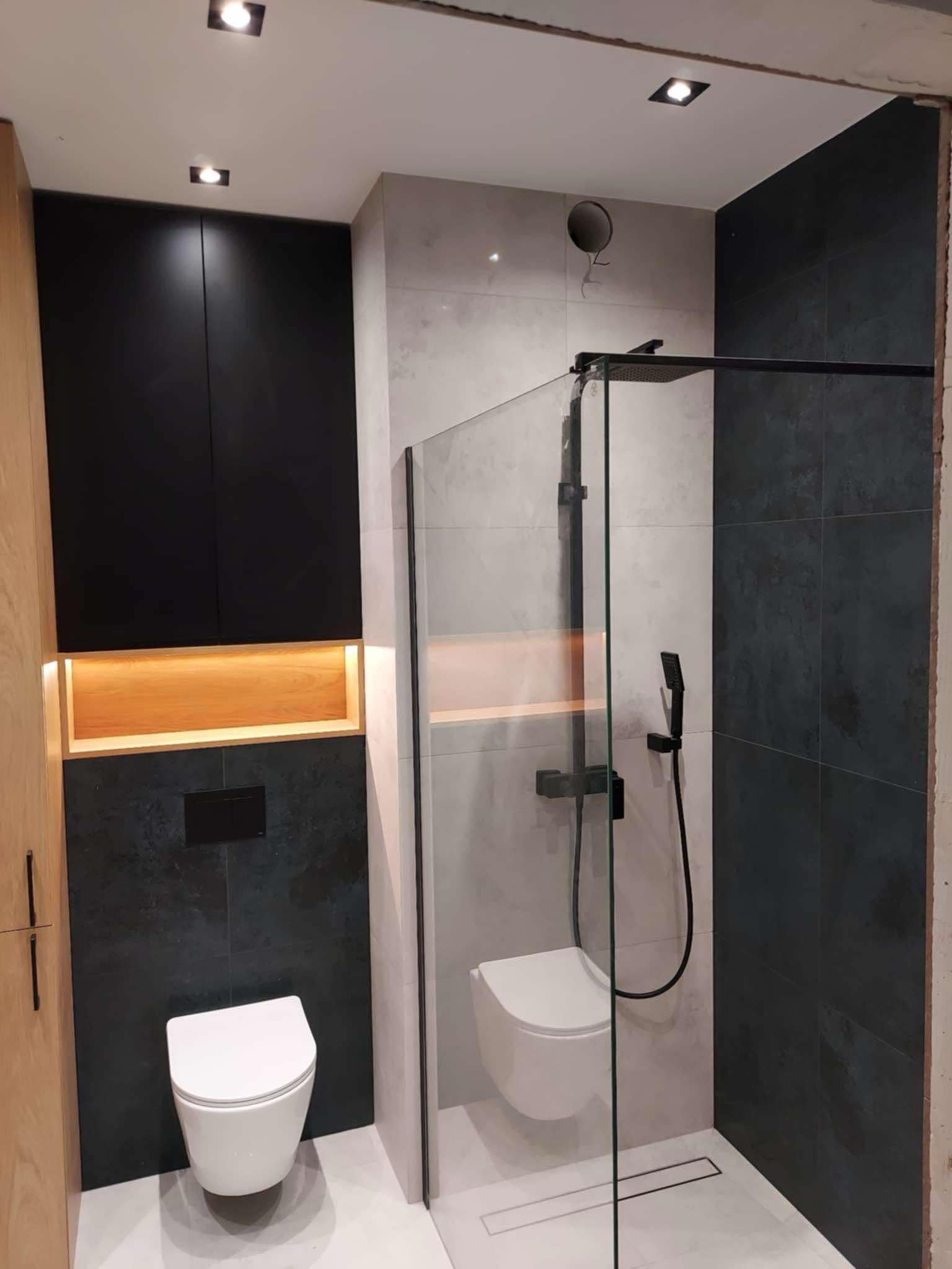 Nowoczesna łazienka z kabiną prysznicową typu walk-in, wiszącą toaletą i szafkami w kolorze czarnym z oświetleniem ambientowym wnęki.