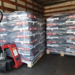 Wnętrze naczepy z paletami worków z ekogroszkiem, zabezpieczonych folią stretch, z widocznym wózkiem paletowym.