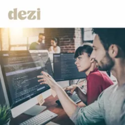 Dwoje programistów analizuje kod na monitorze, z karteczką 'visual design' przyklejoną do ramki monitora, w tle widoczni inni pracownicy biura.