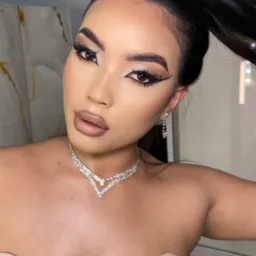 Portret kobiety z wyrazistym, graficznym eyelinerem, nude ustami i upiętymi włosami, prezentującej stylizację z biżuterią.