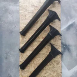 Cztery czarne, metalowe słupki balustrady ułożone ukośnie na płycie OSB, widoczne detale dekoracyjne i wykończenie.