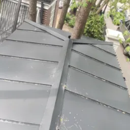 Szary dach z blachy na budynku, z drzewem wyrastającym przez otwór w pokryciu, widok z góry.