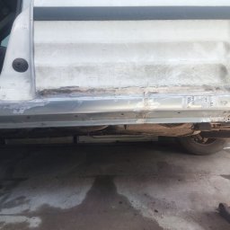 Yarmar Marta Fedoriv - Naprawa progu białego samochodu w warsztacie. Widoczne ślady spawania i obróbki blacharskiej. Dolna część karoserii po naprawie, z widocznymi elementami podwozia.