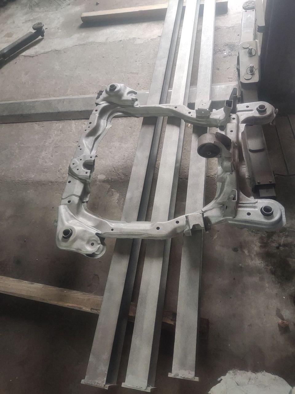 Element podwozia po piaskowaniu i malowaniu, leżący na metalowych profilach. Szary, matowy kolor. Widoczne ślady obróbki.