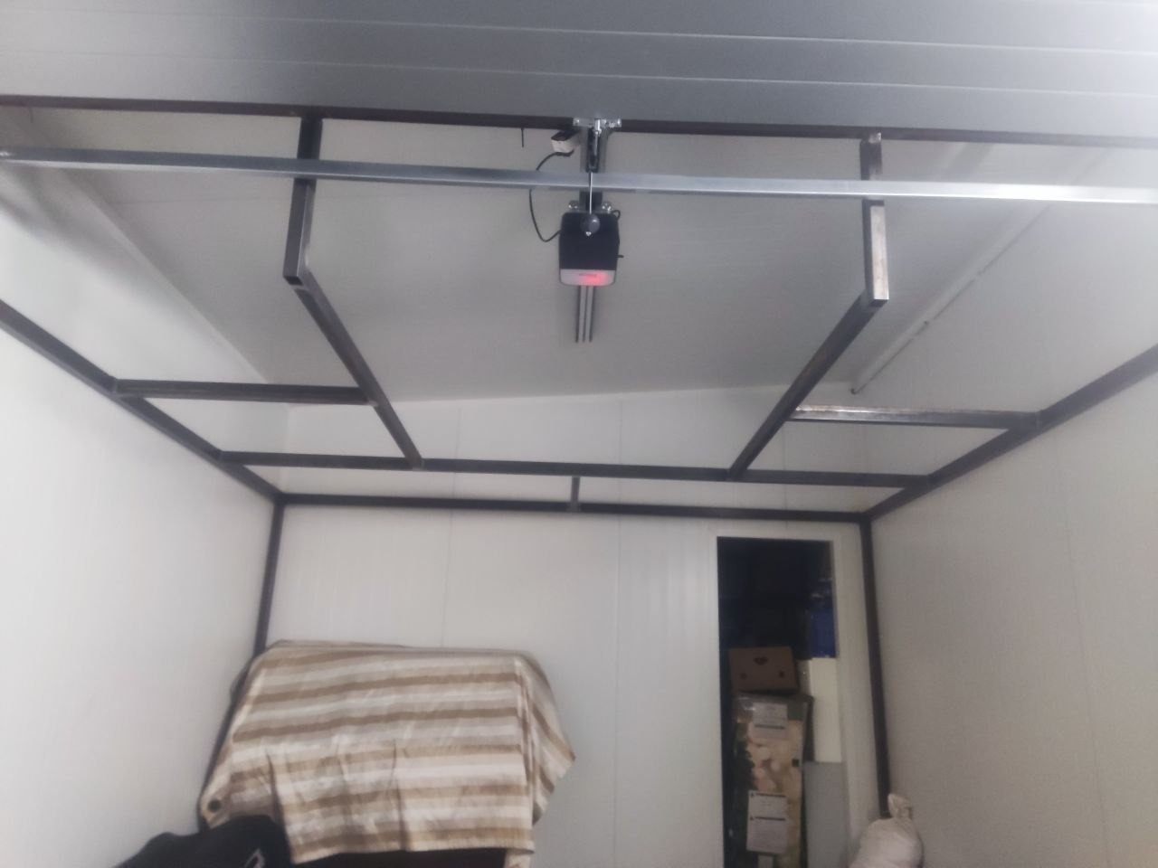 Wnętrze chłodni w trakcie budowy: metalowa konstrukcja ramy, białe panele ścienne, widoczny mechanizm sufitowy. Ujęcie z dołu, surowy stan.