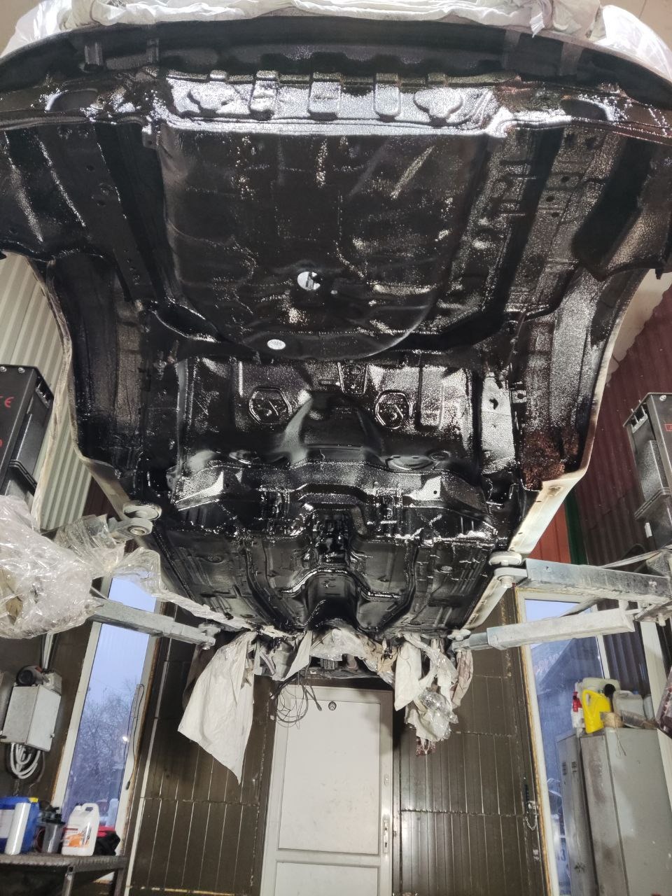 Podwozie auta po nałożeniu czarnej powłoki ochronnej, widoczne na podnośniku w warsztacie. Detal: świeża, błyszcząca warstwa zabezpieczająca przed korozją.