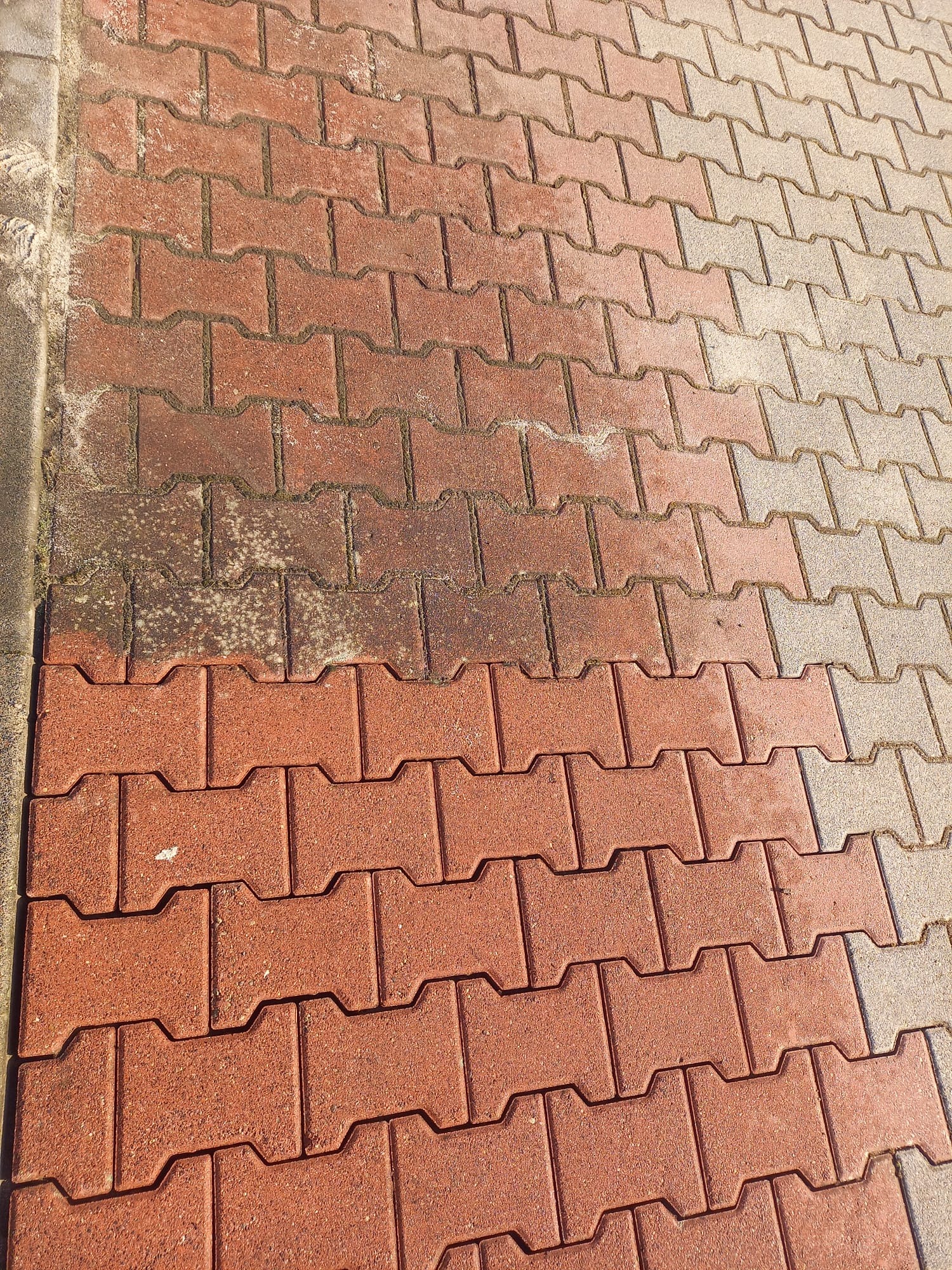 Częściowo wyczyszczona, czerwona kostka brukowa typu I. Widoczna różnica w kolorze i czystości między umytą a brudną powierzchnią. Kątowy widok z góry.