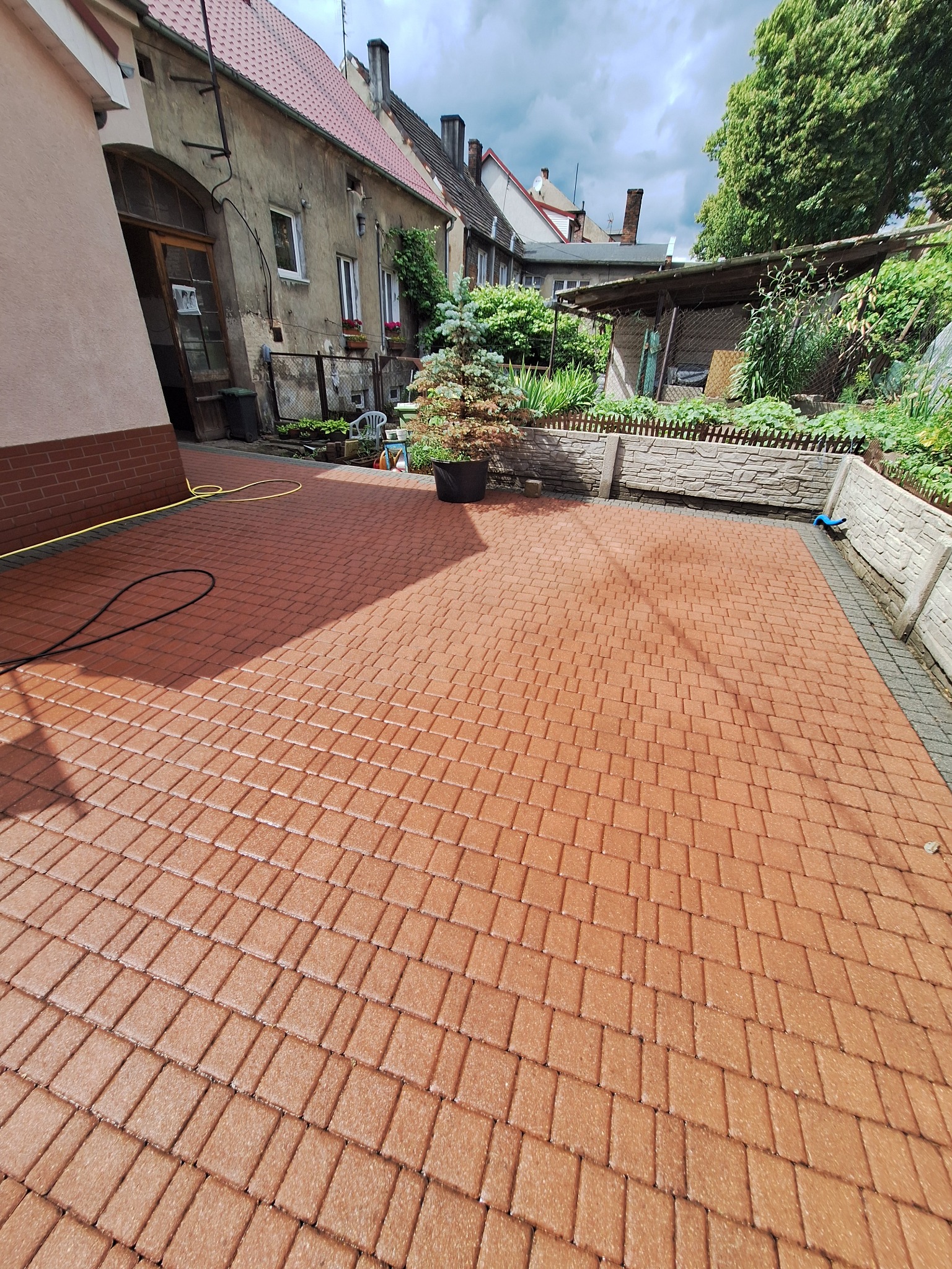 Czysta, brązowa kostka brukowa po umyciu w Szczecinie. Widoczne budynki w tle i wąż do mycia. Świeżo umyta powierzchnia kostki.