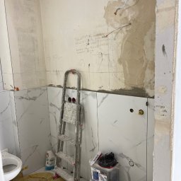 Profesjonalne wykończenia wnętrz Łukasz Szulc - Remont łazienki w trakcie: ułożone marmurowe płytki częściowo zakrywają ściany z instalacją elektryczną i notatkami, drabina monterska oparta o ścianę, widoczne narzędzia i materiały budowlane.