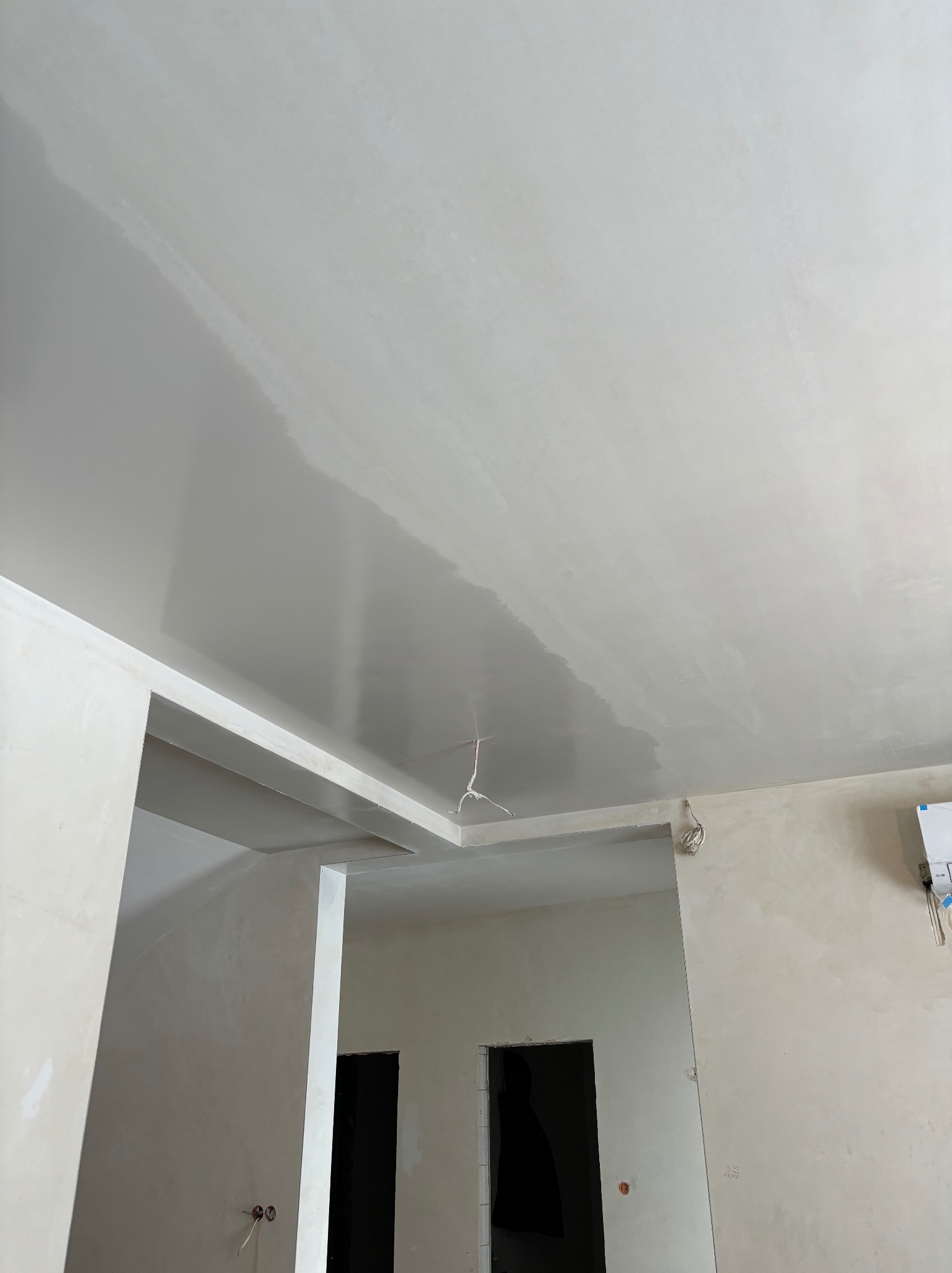 Świeżo nałożona, lekko połyskująca gładź na suficie w trakcie schnięcia, widoczne niedoskonałości i refleksy światła, surowe wnętrze w trakcie prac wykończeniowych, wystające przewody elektryczne.