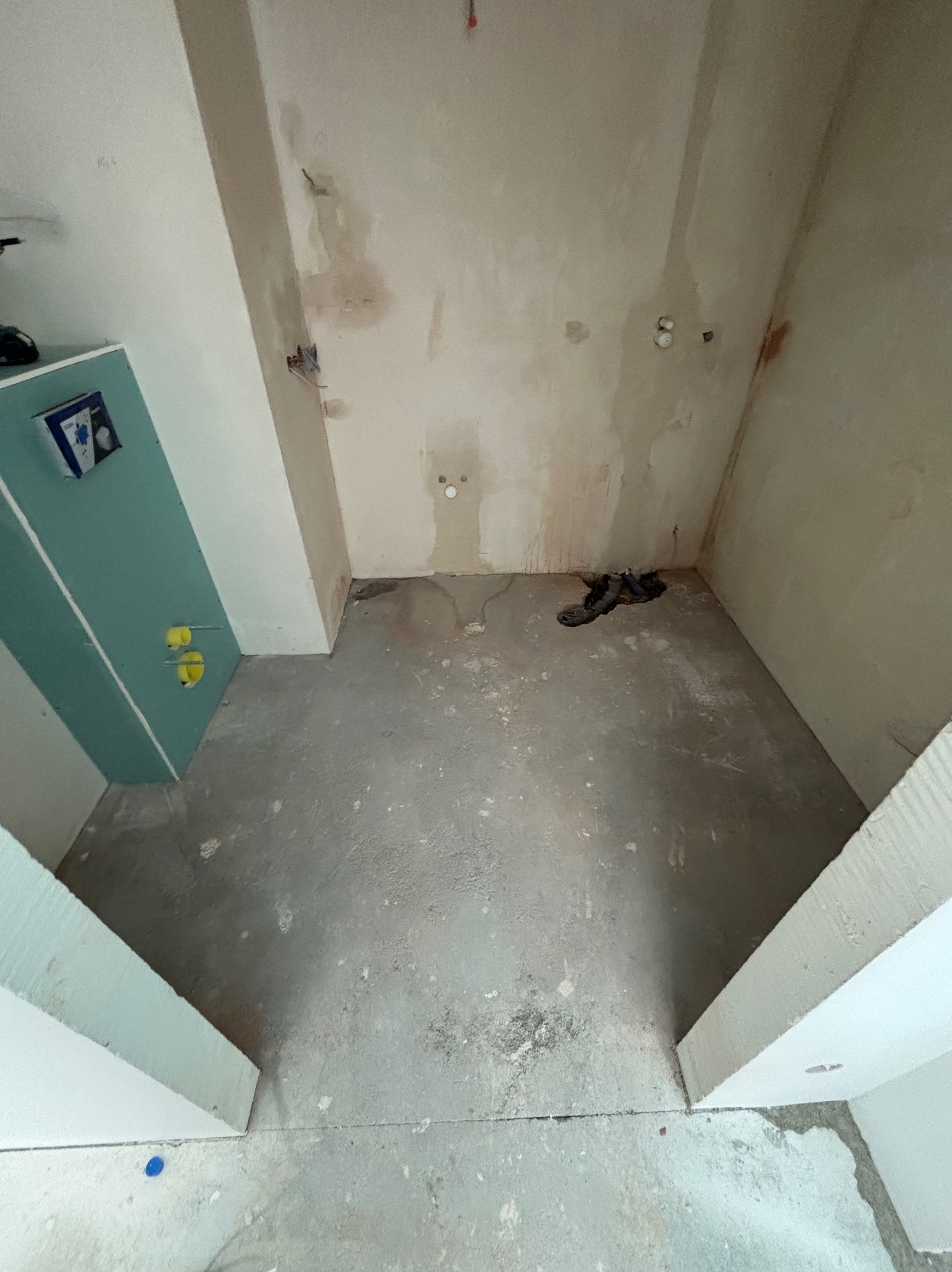 Surowy stan łazienki w trakcie prac: ściany bez wykończenia, widoczne instalacje, surowy beton na podłodze, płyta karton-gips z elementami instalacji wodnej.