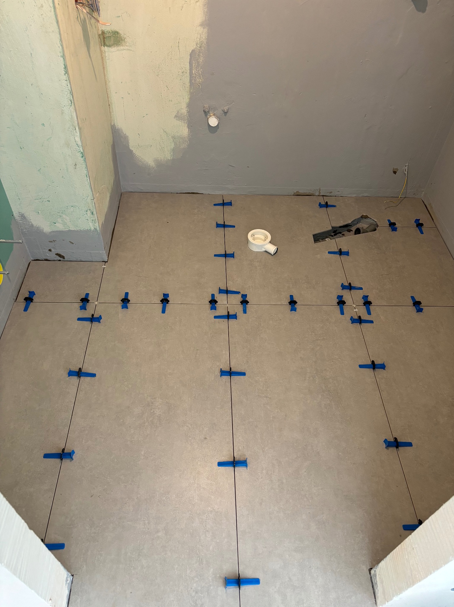 Układanie płytek podłogowych w łazience w trakcie prac, widoczne krzyżyki dystansowe i poziomice, przygotowany odpływ liniowy.