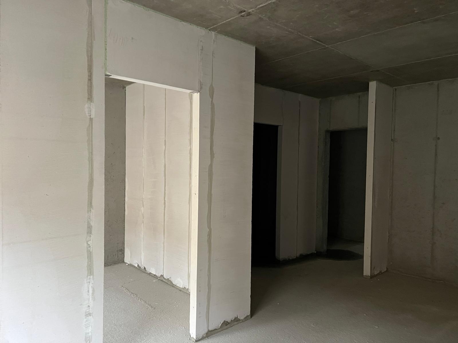 Wnętrze w stanie surowym z panelami Ytong, widoczne surowe ściany i betonowa podłoga. Ujęcie z perspektywy podłogi, widoczne otwory drzwiowe.