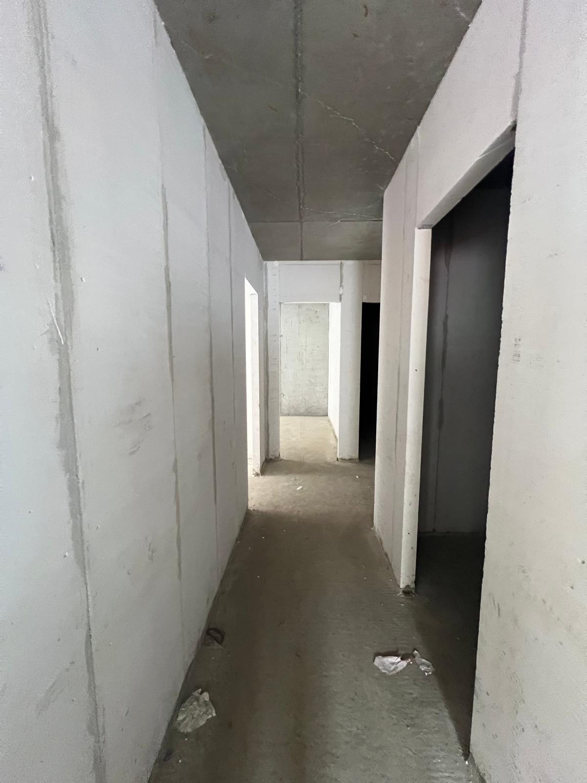 Wnętrze surowego budynku w trakcie budowy. Widoczne ściany z paneli Ytong, surowy betonowy strop i korytarz z otworami drzwiowymi. Minimalistyczny, industrialny charakter.