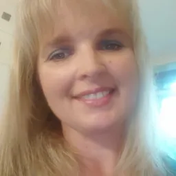 Portret uśmiechniętej blondynki z lekkim makijażem oczu, wykonany w jasnym wnętrzu.