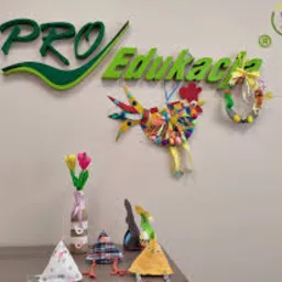 Dekoracje wykonane z materiałów recyklingowych: kogut z kolorowych guzików, wianek z makaronu, tulipany w wazonie z butelki, kukiełki i czapeczka z materiału na tle logotypu firmy edukacyjnej.