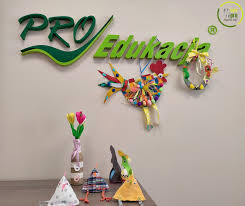 Dekoracje wykonane z materiałów recyklingowych: kogut z kolorowych guzików, wianek z makaronu, tulipany w wazonie z butelki, kukiełki i czapeczka z materiału na tle logotypu firmy edukacyjnej.