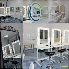 Sala szkoleniowa z lustrami do makijażu z oświetleniem LED, krzesła barowe, stanowiska pracy z kosmetykami, logo firmy na ścianie.