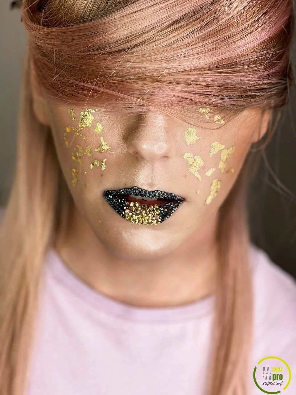 Portret kobiety z artystycznym makijażem: złote płatki na twarzy i usta zdobione czarnymi i złotymi kryształkami.