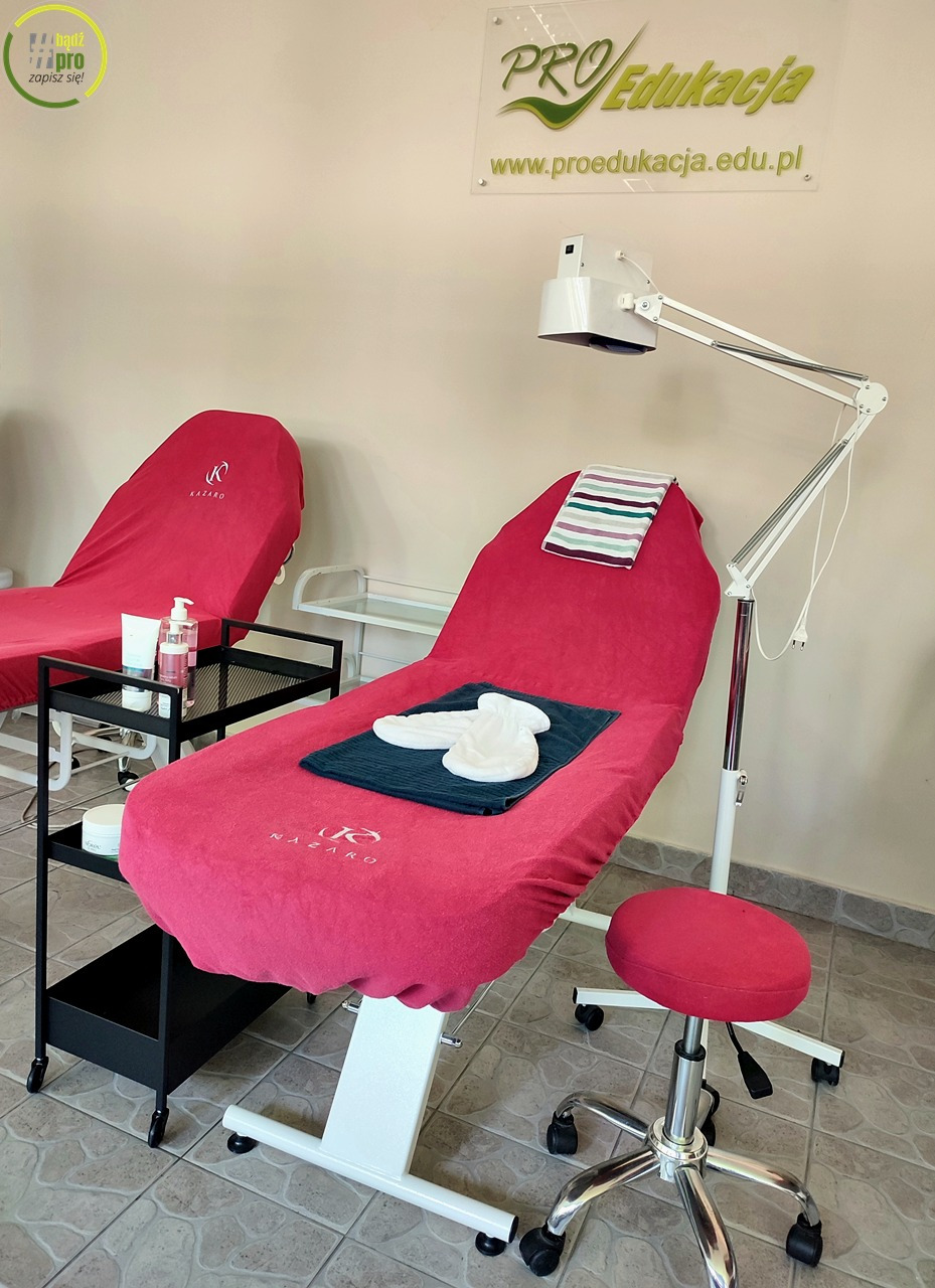 Gabinet kosmetyczny z dwoma leżankami przykrytymi różowymi pokrowcami z logo, lampą kosmetyczną i stołkiem na kółkach. Na jednej leżance ręcznik i jednorazowe klapki.