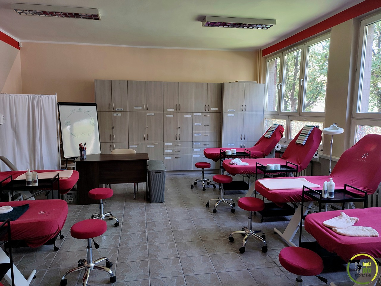 Sala szkoleniowa z kilkoma stanowiskami do ćwiczeń, tablicą suchościeralną z rysunkiem koła i szafkami w tle.