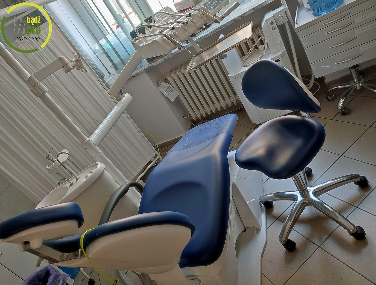 Nowoczesny unit stomatologiczny z niebieskim obiciem, widok z perspektywy pacjenta, oświetlenie dzienne z okna.