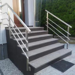 Zewnętrzne schody z szarego granitu z nowoczesną balustradą ze stali nierdzewnej o minimalistycznym designie, widok z dołu, zieleń w tle.