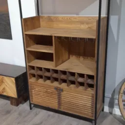 Drewniany regał z metalową ramą, zawierający półki, uchwyty na kieliszki, przegródki na butelki i szafkę z lamelkowymi drzwiczkami.