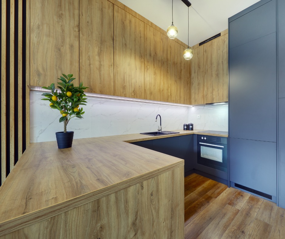 Nowoczesna kuchnia z drewnianymi frontami szafek górnych i blatem, ciemnoszarymi szafkami dolnymi i sztuczną rośliną cytryny na blacie.