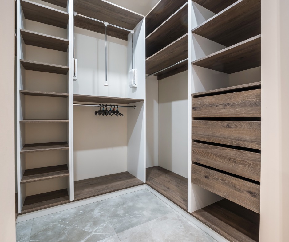 Przestronna garderoba z szufladami i półkami z drewna w odcieniach brązu, zrealizowana w Gołotach. Widoczne metalowe drążki na wieszaki i szare płytki na podłodze.