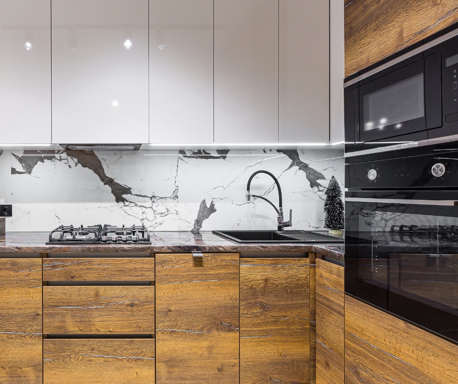 Nowoczesna kuchnia z drewnianymi frontami szafek dolnych, białymi szafkami górnymi i blatem imitującym marmur. Na blacie czarny zlew i płyta gazowa.