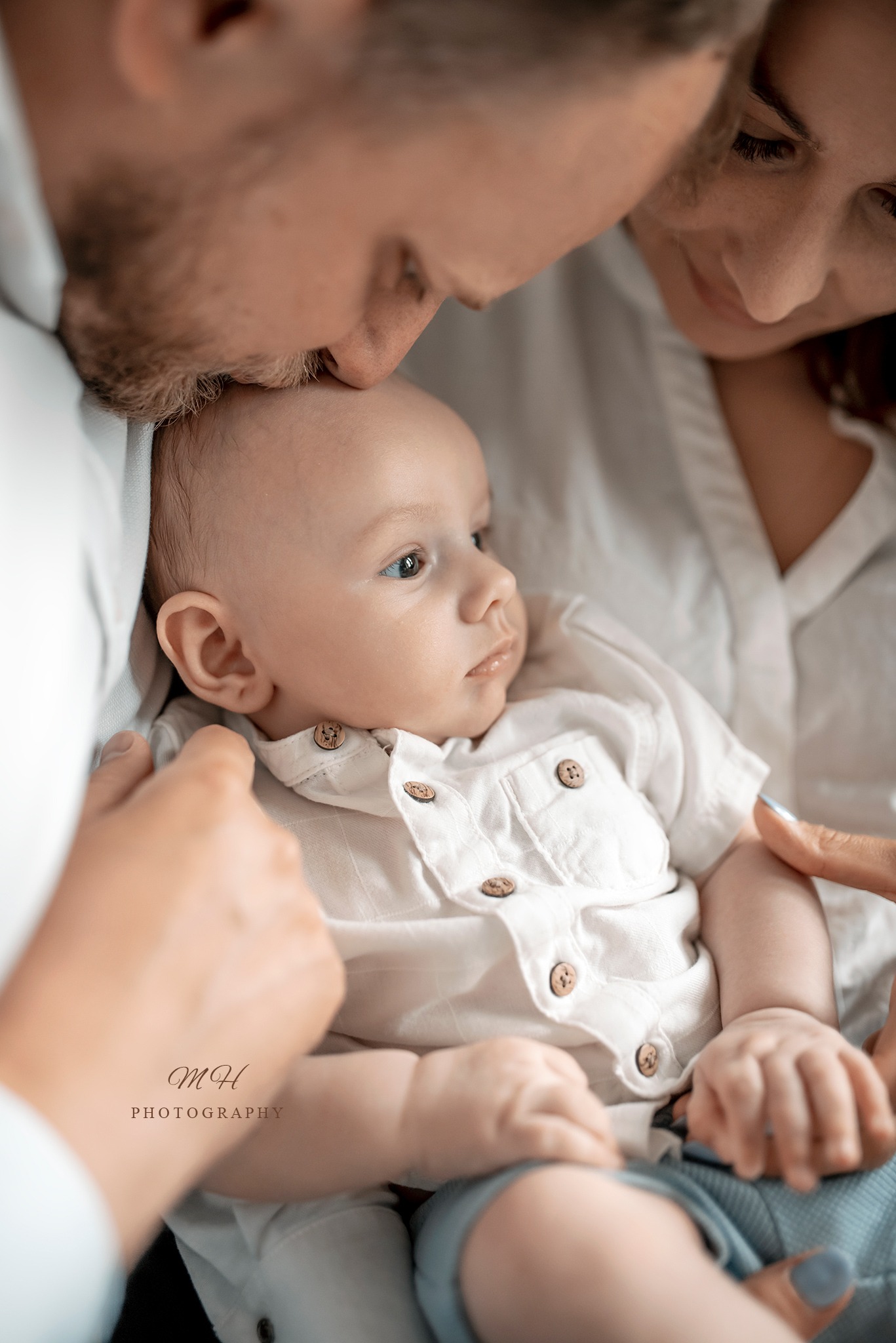 Rodzice otulają noworodka w jasnych ubraniach, delikatne światło podkreśla bliskość i miłość.