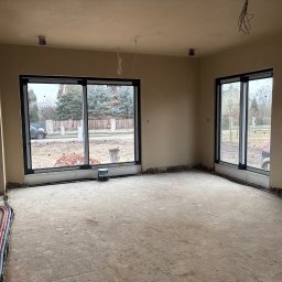 Bud-Pat - Wnętrze domu w stanie deweloperskim po tynkowaniu maszynowym ścian i sufitu, widoczne wystające przewody elektryczne, przygotowane do dalszych prac wykończeniowych.