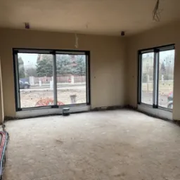 Wnętrze domu w stanie deweloperskim po tynkowaniu maszynowym ścian i sufitu, widoczne wystające przewody elektryczne, przygotowane do dalszych prac wykończeniowych.