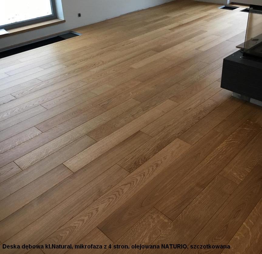 Ułożona dębowa podłoga w odcieniach naturalnego drewna, wykończona olejem, z mikrofazą na czterech stronach, widoczne szczotkowanie i fragment kominka.