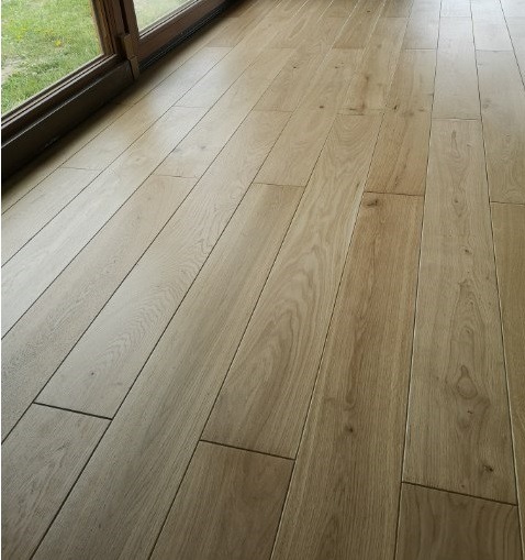 Jasna, parkietowa podłoga ułożona równolegle do okna balkonowego z brązowymi ramami, widok z góry pod kątem.