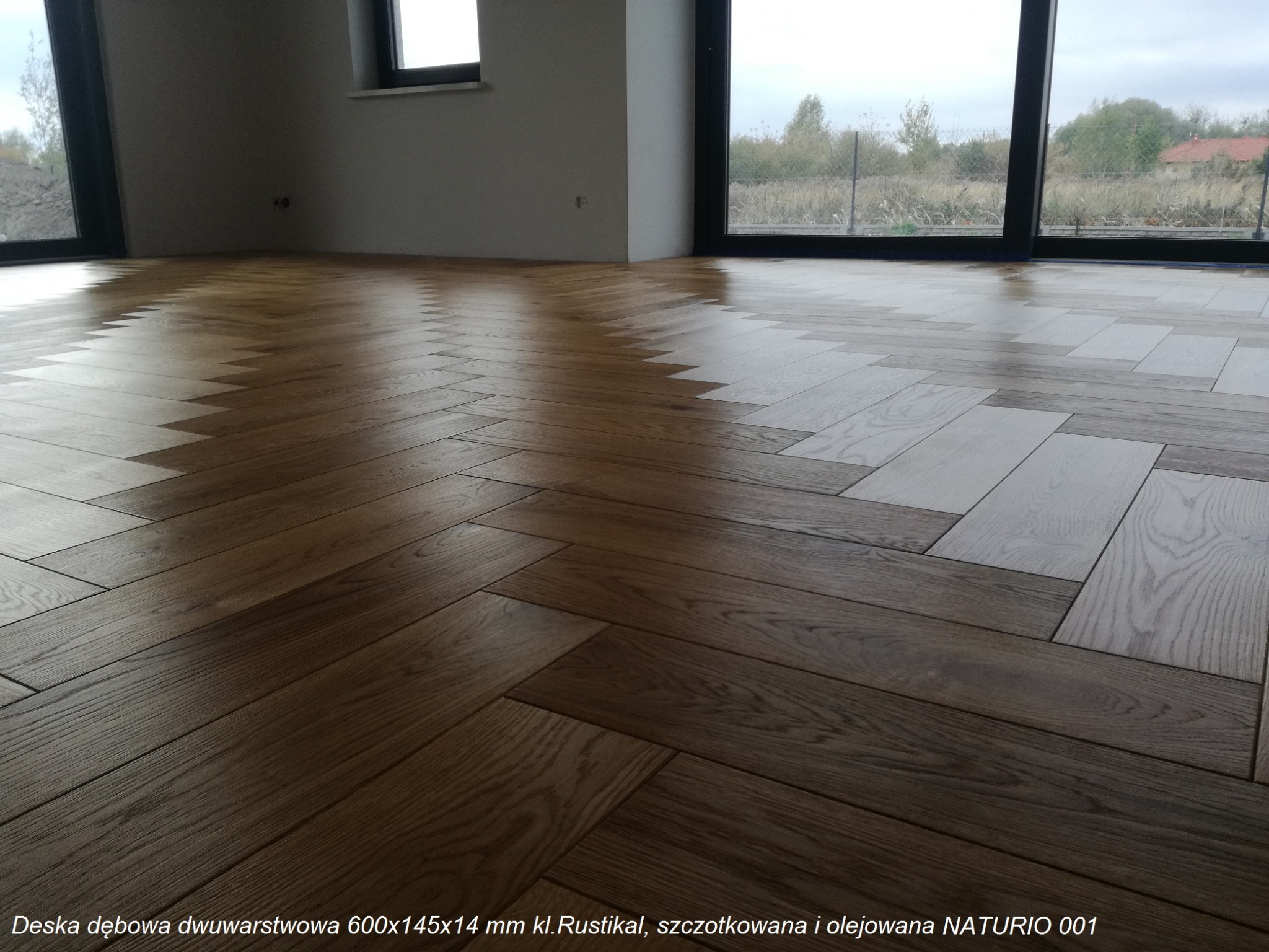 Ułożona w jodełkę, dwuwarstwowa deska dębowa, szczotkowana i olejowana w Hajnówce. Widoczne okno z widokiem na zewnątrz.