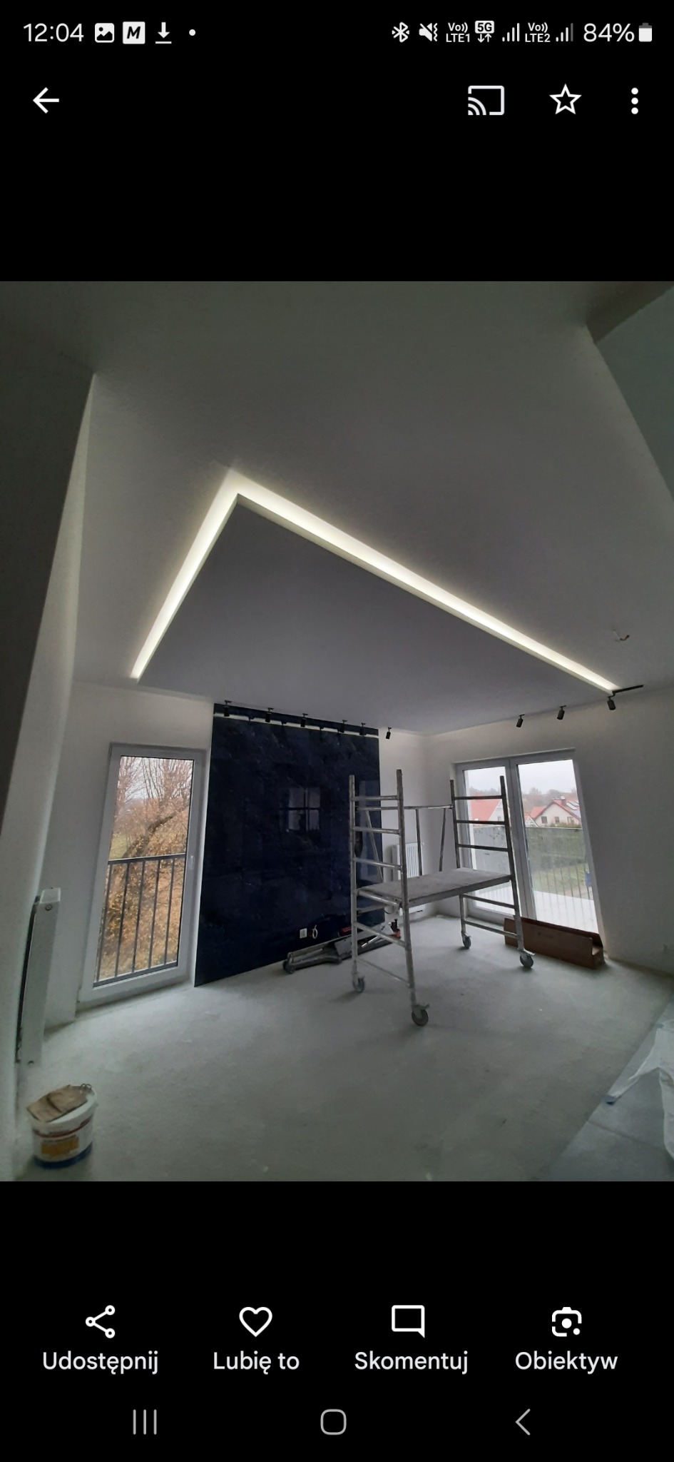 Nowoczesne wykończenie wnętrza: podwieszany sufit z oświetleniem LED, ciemna ściana z oknem, rusztowanie w pokoju. Etap prac wykończeniowych.