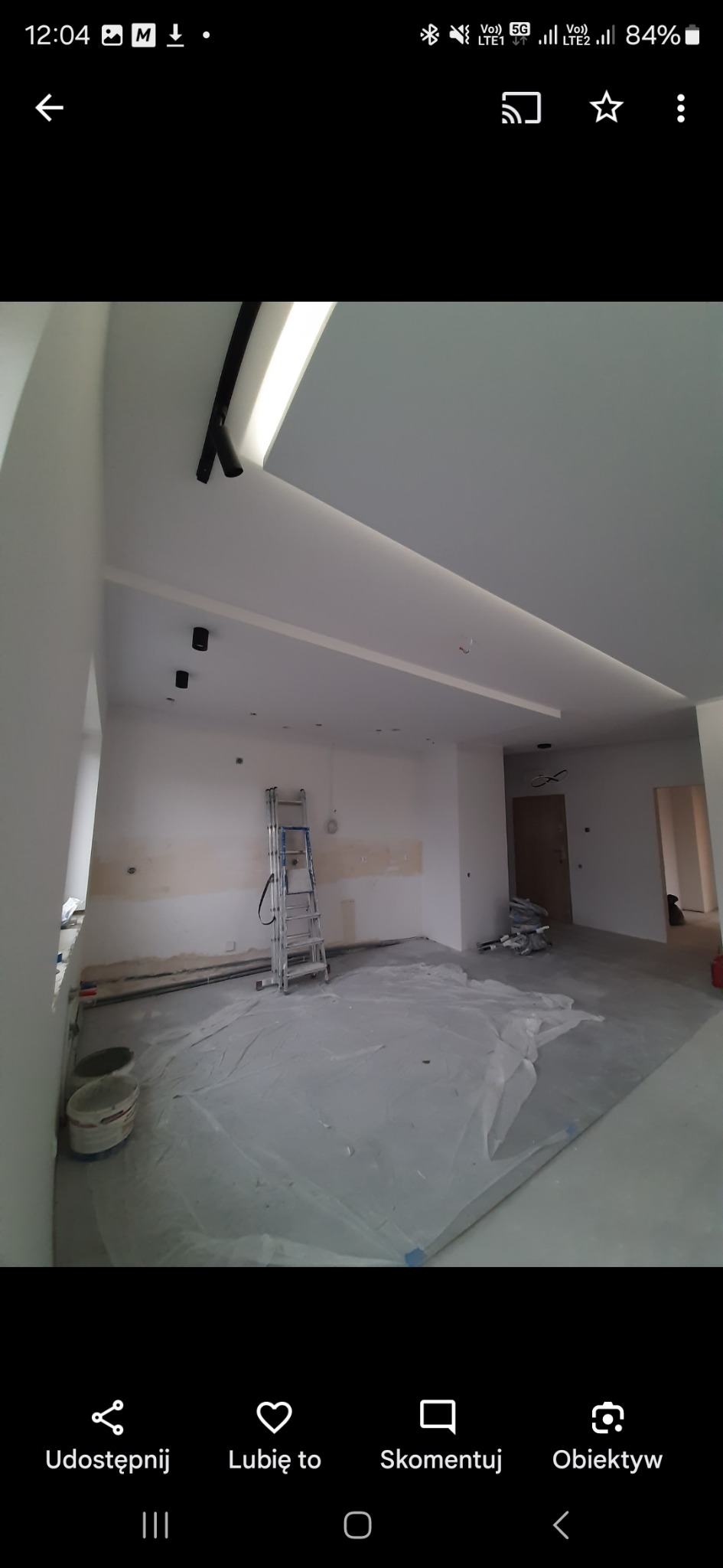 Wnętrze w trakcie prac wykończeniowych: zabezpieczona folią podłoga, ściany przygotowane do malowania, widoczna drabina i oświetlenie sufitowe.