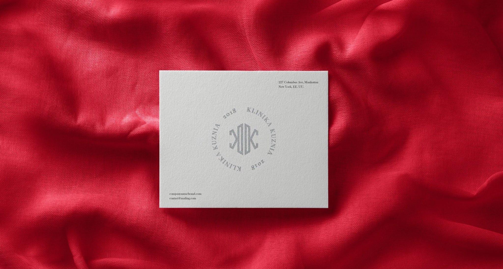 Elegancka wizytówka firmy Klinika Kuznia z monogramem i adresem na tle czerwonej, drapowanej tkaniny.