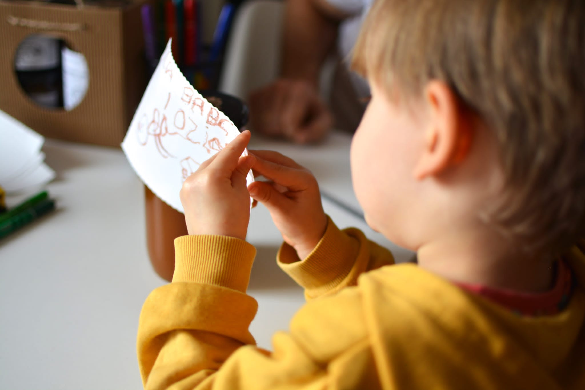 Chłopiec w żółtej bluzie przykleja kartkę z rysunkami do słoika z miodem, widoczne ręcznie wykonane etykiety.