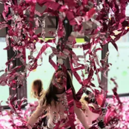 Dziewczynka w różowo-srebrnym deszczu konfetti, uśmiechnięta, z gwiazdką na czole podczas imprezy urodzinowej, w tle widoczna inna postać.